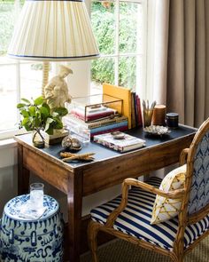 a desk with a lamp, chair and books on it in front of a window