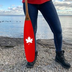 a woman standing on the beach holding a paddle with an island flag painted on it