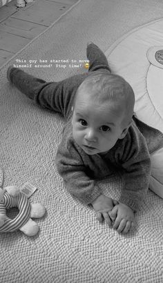 a baby laying on the floor next to a stuffed animal and some toy animals in black and white