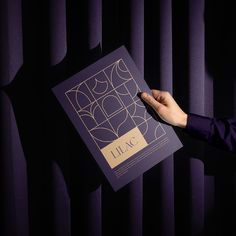 a person is holding up a book in front of the curtained room with purple curtains