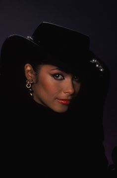 a woman wearing a black hat with big hoop earrings on her head and dark background