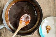 a wooden spoon with some liquid in it on a table next to another bowl and plate