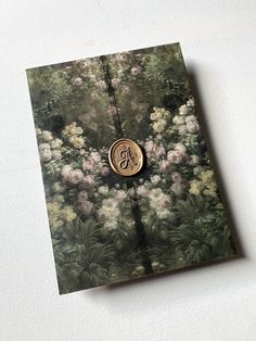 an open book with flowers on it and a monogrammed button in the middle