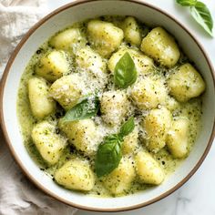 a white bowl filled with ravioli and pesto on top of a marble counter