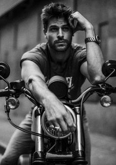 a black and white photo of a man sitting on a motorcycle with his hand on the handlebars