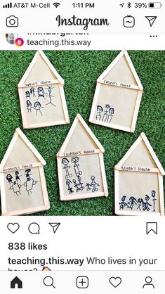 four wooden houses with family drawings on them sitting in the grass, one is for children's house