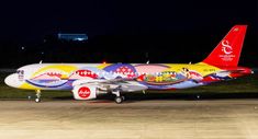 a brightly colored plane is parked on the tarmac at night with its lights on