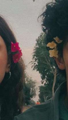 two people with flowers in their hair standing next to each other and looking at the camera