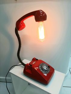 an old fashioned red telephone sitting on top of a white table next to a light bulb