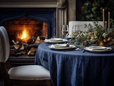 a table set for two with plates and wine glasses in front of a fire place