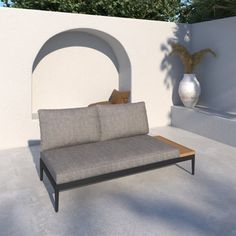 a couch sitting on top of a cement floor next to a white wall and potted plant