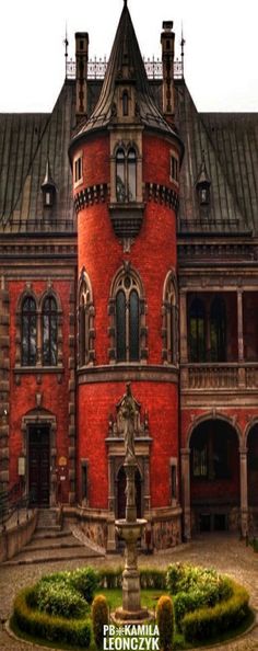 a large red brick building with a fountain in front of it and bushes around the perimeter