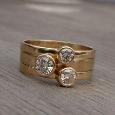 two gold wedding rings with three diamonds on each one, sitting on a wooden surface