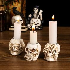 three white candles with skulls on them sitting on a wooden table next to other halloween decorations