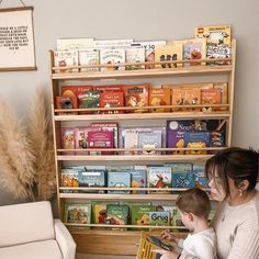 a woman holding a baby in front of a bookshelf filled with children's books