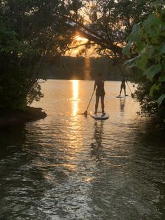 two people on paddle boards paddling down a river at sunset with the sun setting behind them