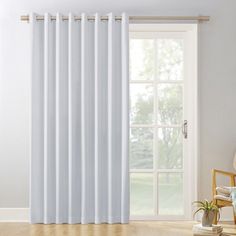 a white curtain hanging on the side of a window next to a chair and potted plant