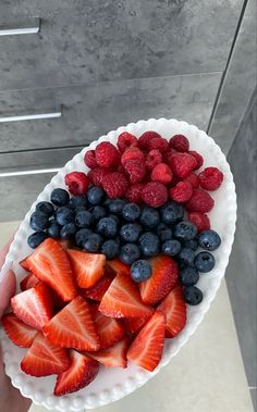 a person holding a white plate with strawberries and blueberries on it in front of a gray wall