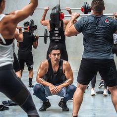 a group of men and women in a gym doing squat exercises with barbells