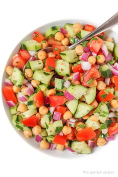 a white bowl filled with cucumber, tomato and chickpea salad next to a spoon