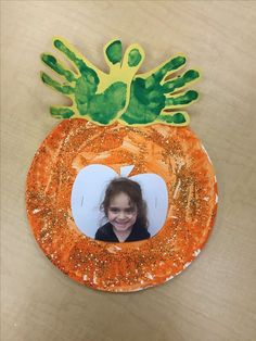 a child's handprinted photo in the center of a paper plate pumpkin