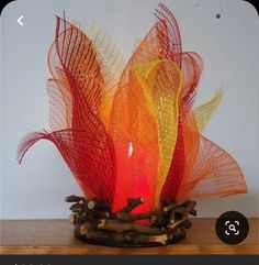 an orange and yellow vase sitting on top of a wooden table next to a white wall