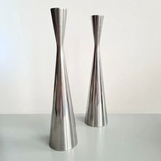 two tall silver vases sitting on top of a white table next to each other