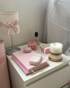 a white dresser topped with pink items next to a lamp