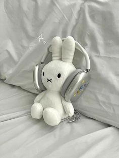 a white stuffed rabbit with headphones on it's ears sitting on a bed