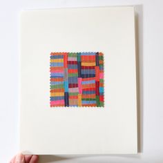 a person holding up a piece of art made out of colored strips