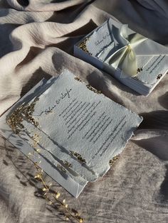 two wedding cards with gold confetti on them are laying on a bed sheet