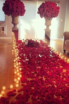 red rose petals on the ground with candles in front of them and two vases filled with flowers