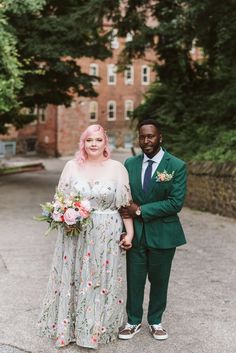 a man in a green suit standing next to a woman wearing a floral dress and holding hands