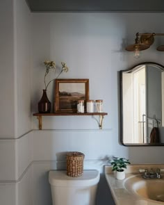 a white toilet sitting next to a sink in a bathroom under a mirror and a wooden shelf