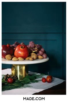 a cake stand with apples, grapes and nuts on it in front of a blue wall