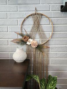 a white vase sitting on top of a wooden table next to a wall hanging with flowers