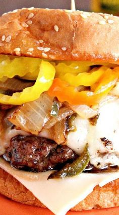 a cheeseburger with onions, peppers and mushrooms on a toasted bread bun