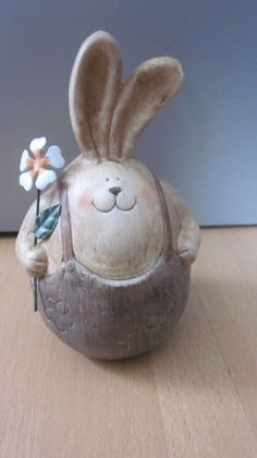 a ceramic bunny holding a flower on top of a wooden table next to a wall