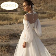 a woman in a white wedding dress standing on a dirt road with her back to the camera