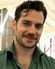 a close up of a person wearing a green shirt and smiling at the camera with a building in the background