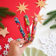 a person is holding up some colorful paper scissors in front of snowflakes and christmas decorations