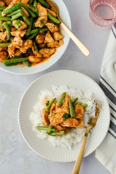 two plates with chicken and asparagus on rice next to a glass of water