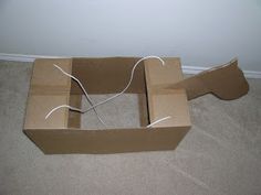 an open cardboard box sitting on the floor next to a wall with wires in it