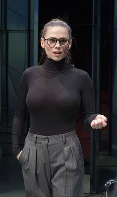 a woman in black shirt and grey pants with hand out to the side while wearing glasses