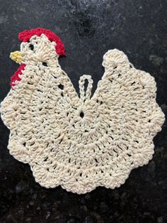 a crocheted chicken sitting on top of a black table next to a red and white object