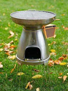 a large metal grill sitting on top of a lush green grass covered park next to leaves