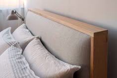 a bed with white pillows and wooden headboard next to a lamp on the wall