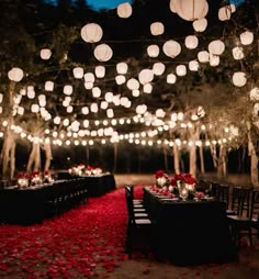 an outdoor dinner setup with paper lanterns and red rose petals on the ground at night