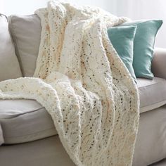 a white crocheted blanket sitting on top of a couch next to two pillows