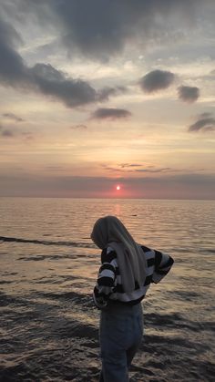 a person standing on the beach at sunset with their head in his hands, looking out into the ocean